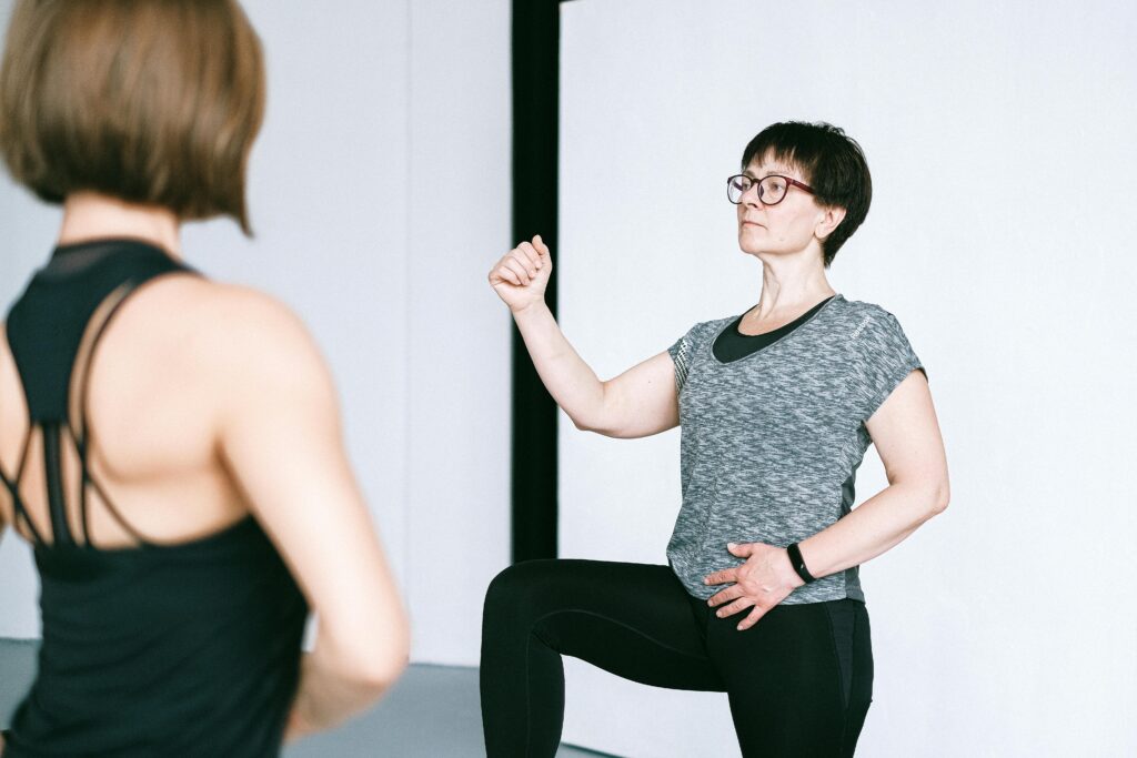 A woman practicing yoga indoors with a fitness instructor providing guidance.
